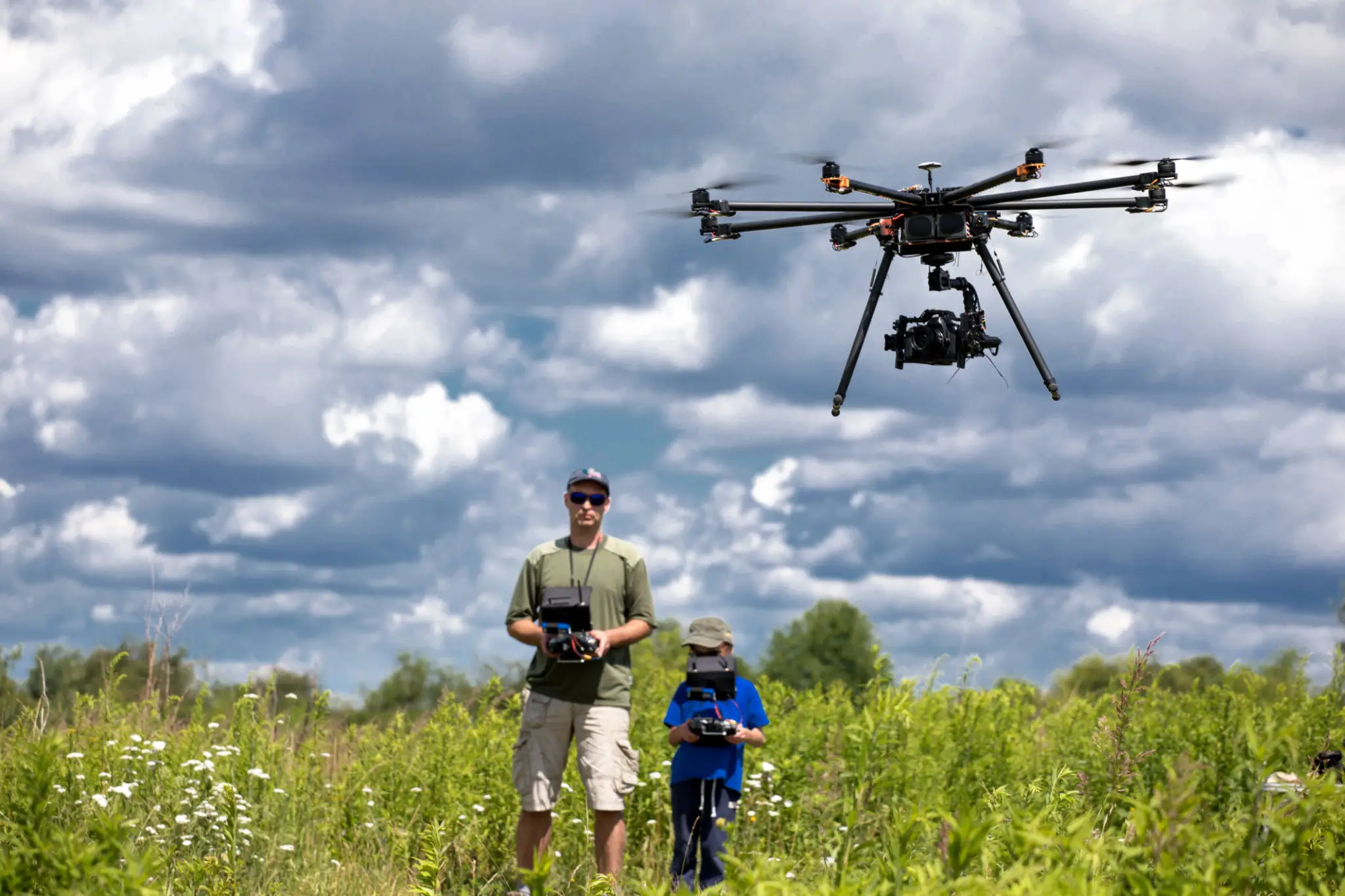 Drone hovering over grassy field, cloudy sky