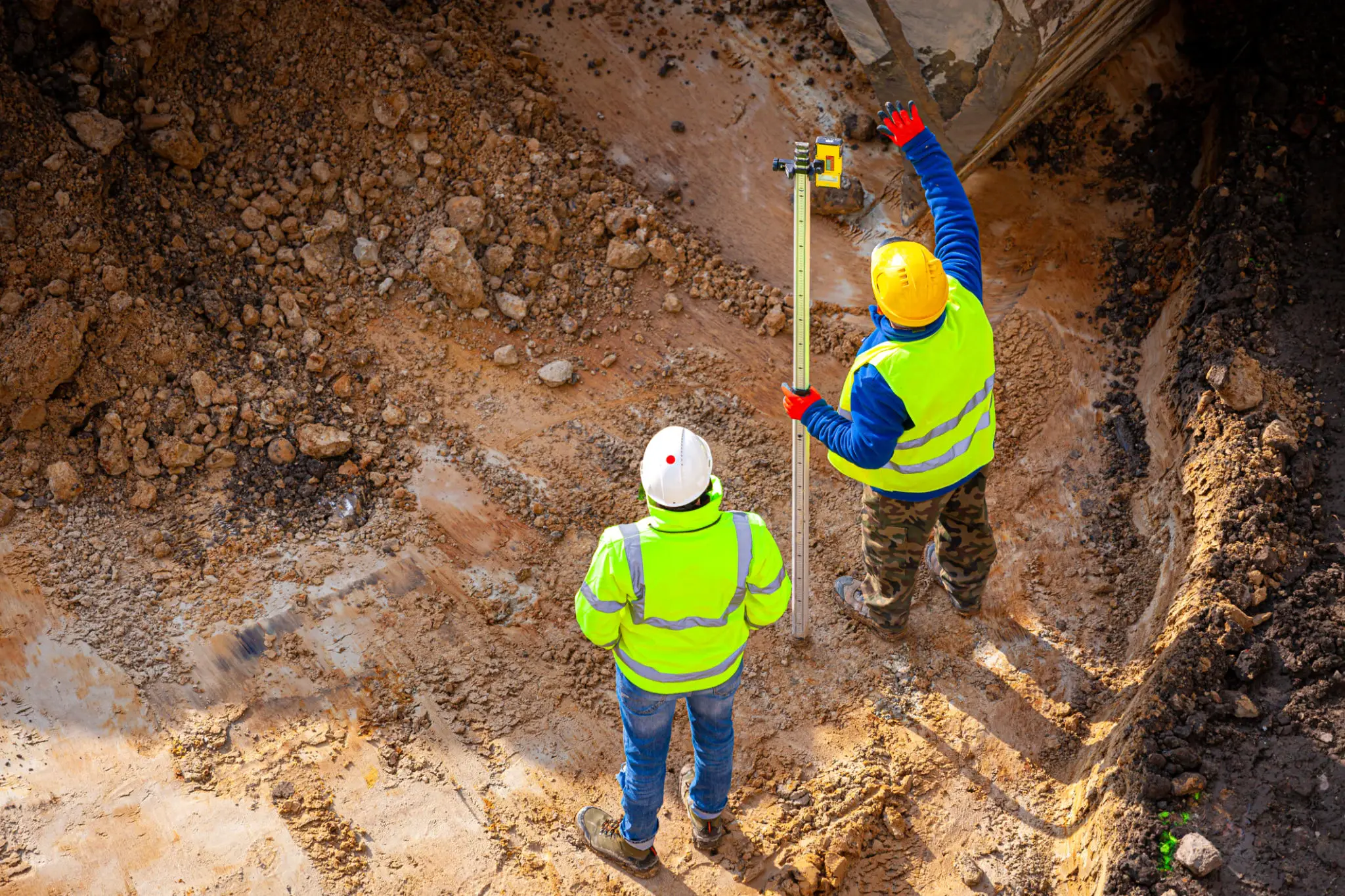 Two builders with measuring tool on dirt