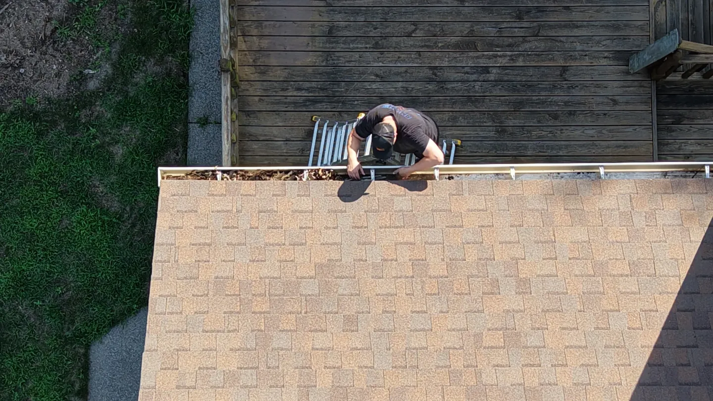 Person cleaning roof gutters from ladder