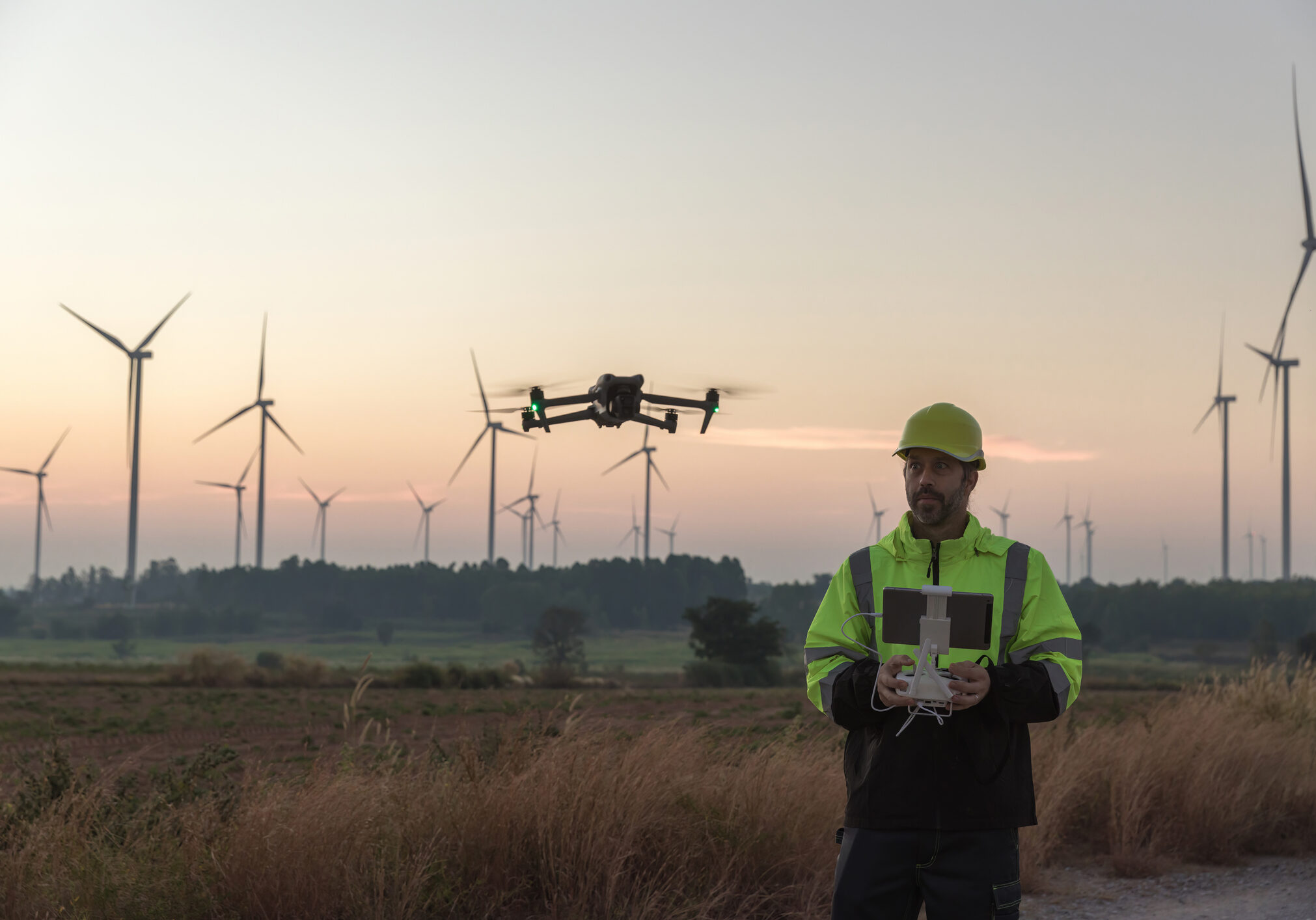Man flying drone by wind turbines